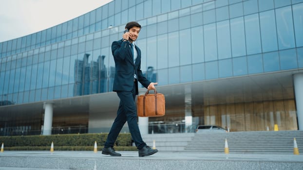 Smart business man using phone to talking while walking at building. Happy manager walking at street while talking on smart phone to discuss business plan or marketing strategy or working. Exultant.