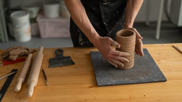 Close-up of a man's hands making a patterned cylinder out of clay