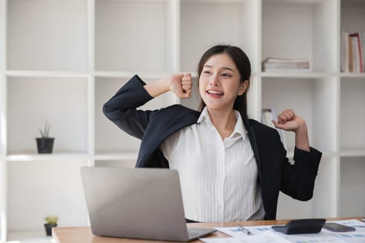 Confident business woman working on a laptop in a modern office, smiling and stretching. Professional female entrepreneur in a productive work environment.