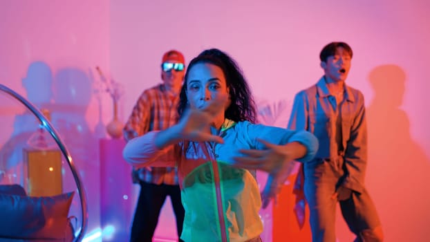 Attractive happy dancer looking at camera while smart woman moving at rhyme with neon light. Professional hispanic performer break dancing while wearing colorful cloth with diverse friend. Regalement.