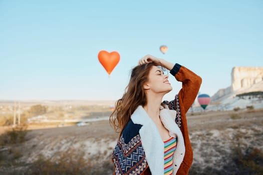 joyful woman surrounded by colorful balloons with heart shaped balloon floating in front of majestic mountain