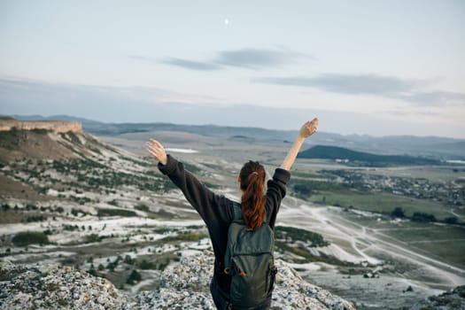 Woman embracing the vast mountain valley below with arms outstretched in awe of the breathtaking view