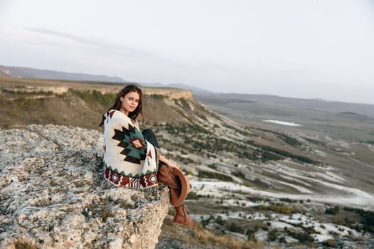 Serene woman sitting on mountain rock with blanket and hat, enjoying peaceful solitude in nature