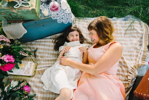 happy mother and daughter playing and smiling while lying on a blanket in the Park in the summer