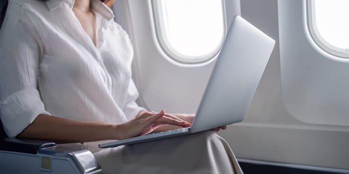 Professional businesswoman working on a laptop during airplane travel, showcasing modern business travel and technology use.