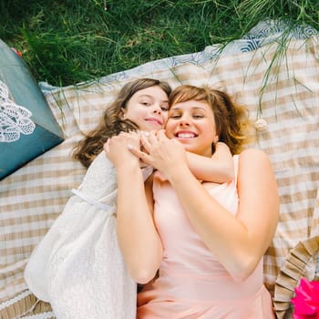 happy mother and daughter hugging lying down on a blanket in the summer on the nature