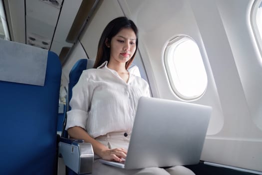Business woman working on a laptop while traveling on an airplane, showcasing modern corporate travel and in-flight productivity.