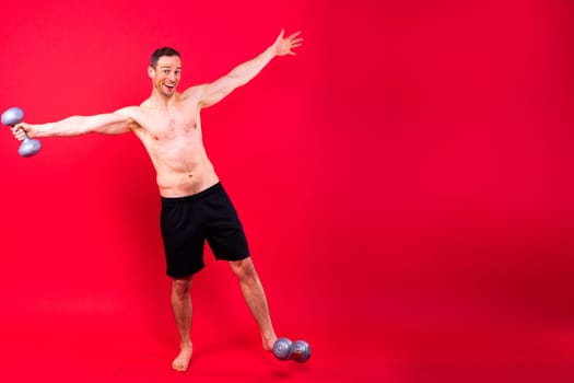 Adult muscular man smiling and screaming while working out hard with a dumbbells.