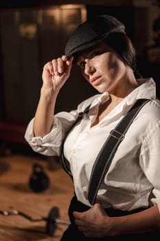 Caucasian woman in a Peaky Blinders style men's suit posing in a retro gym