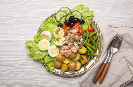 Delicious nicoise salad with tuna, eggs, potatoes, green beans, and olives on white wooden table