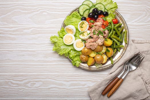 Delicious nicoise salad with tuna, eggs, potatoes, green beans, and olives on white wooden table with copy space