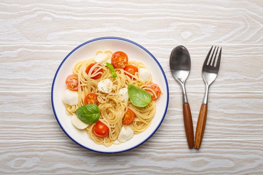 Delicious spaghetti with tomatoes and mozzarella cheese served on white wooden table with cutlery aside, top view