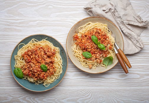 Two plates of delicious spaghetti bolognese with fresh basil leaves, served on a rustic wooden table