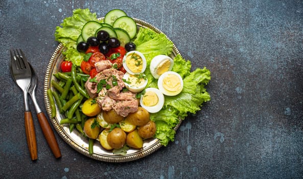Classic French Nicoise salad with tuna, eggs, potatoes, green beans and olives on a silver platter with copy space