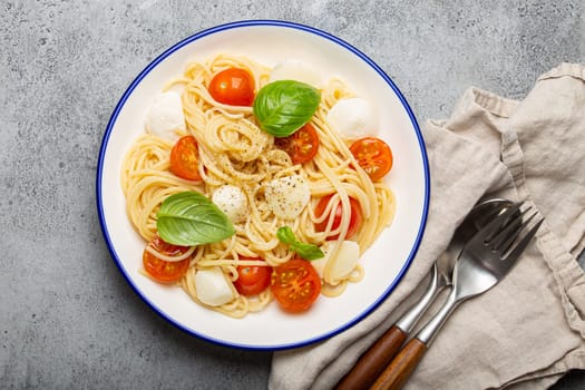 Delicious and fresh spaghetti with cherry tomatoes and mozzarella cheese, seasoned with pepper and basil, served on a plate
