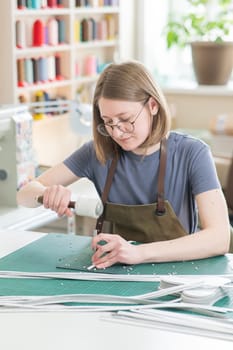 A woman makes holes in a leather belt in a workshop. Vertical photo