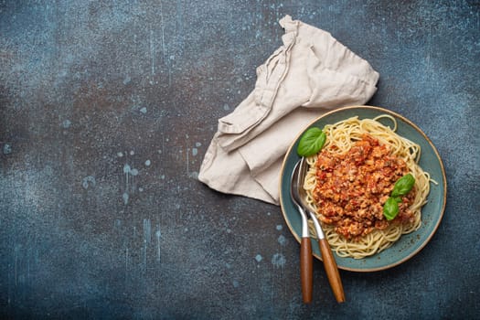 Plate of delicious spaghetti bolognese with fresh basil leaves on dark background with copy space for text