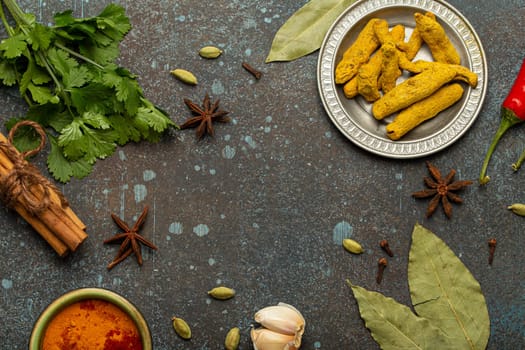 Turmeric root, cinnamon sticks, bay leaves and other spices traditional for Indian cuisine creating a frame on dark background