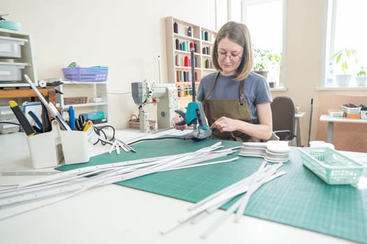 Woman tanner processes the edges of a leather belt in a workshop