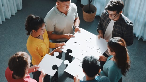 Top view of smart business people put last piece of jigsaw puzzle together to complete puzzle and standing while wearing casual cloth. Group of diverse team finding solution with teamwork. Symposium.