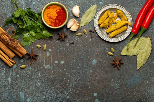 Turmeric root, cinnamon sticks, bay leaves and other spices traditional for Indian cuisine creating a frame on dark background
