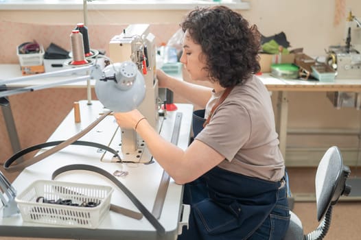 A woman tanner sews a leather belt on a sewing machine