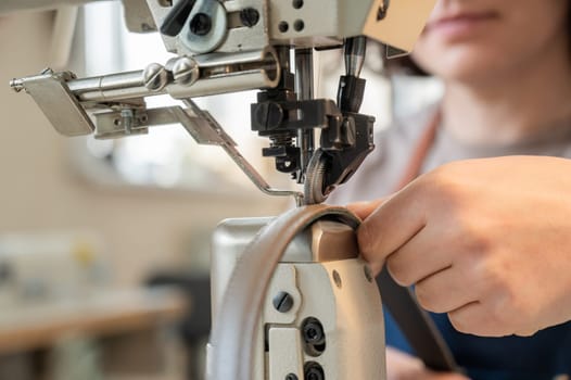 A woman tanner sews a leather belt on a sewing machine