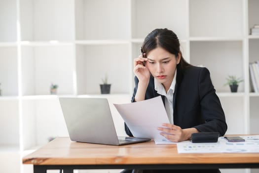 Business woman stressed while working at desk with laptop and documents, experiencing workload pressure.