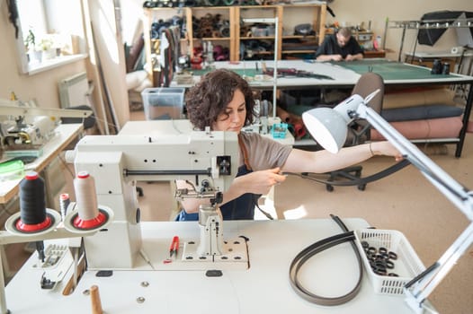 A woman tanner sews a leather belt on a sewing machine