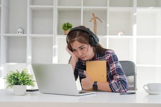 Young woman studying online from home, using a laptop and headphones, in a modern home office setting.