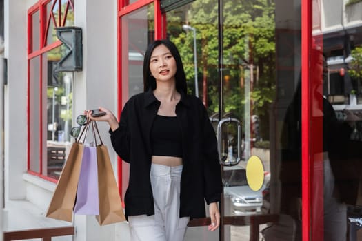 Beautiful young woman enjoying a shopping day, holding bags, and looking stylish in a modern urban setting.