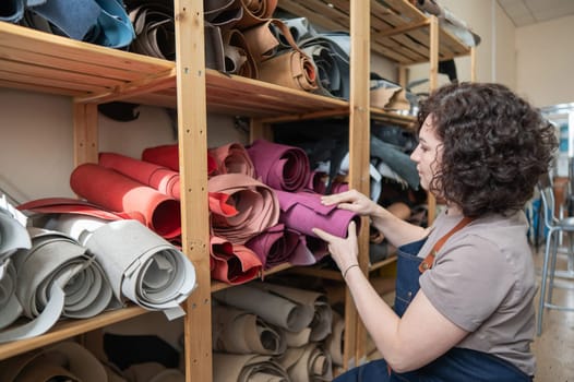 Woman leatherworker selects a roll of leather in the workshop