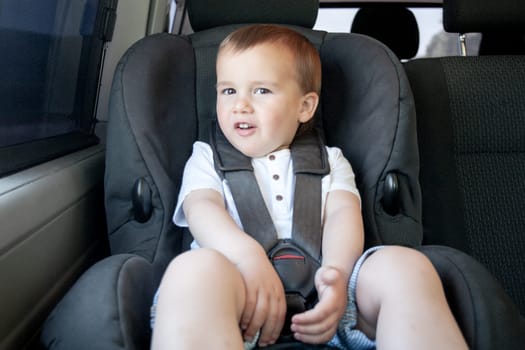 Toddler sitting in child safety seat of car looking at camera. Transportation and safety. 