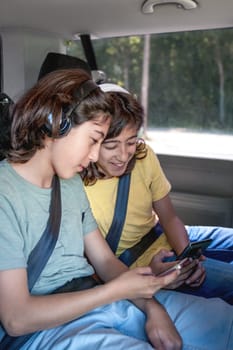 Twin brothers with headphones look at their cell phones while sitting in the van 