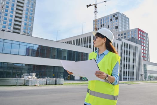 Industrial worker middle aged female builder engineer inspector auditor supervisor with working documents, outdoor construction background. Construction industry service development work concept