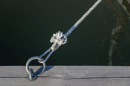 Mooring ring for boats in the port with carbine and black rope from the boat, wooden pier, sunny light, rope knot, Finland