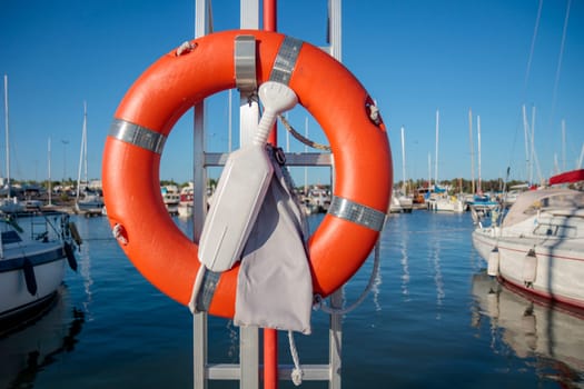 SOS nautical emergency concept. Lifebuoy, orange lifebelt put on vertical ready for using. Close up circle lifesaver buoy at Finnish marina