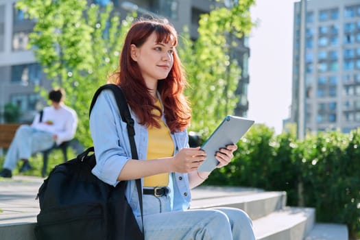Young attractive female college student using digital tablet outdoor, educational building background. Education, technology, training, 19,20 years age youth concept