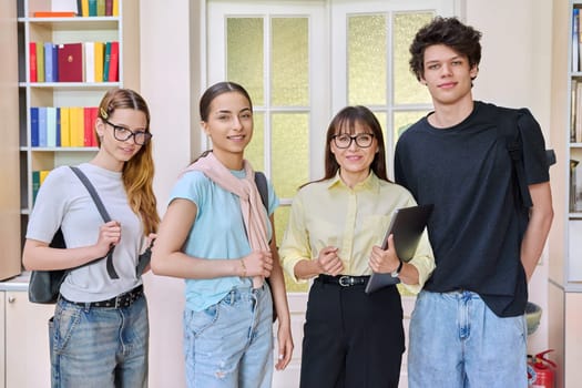 Portrait of group of teenage students with female teacher looking at camera in classroom library. High school, education, adolescence, teaching, learning concept