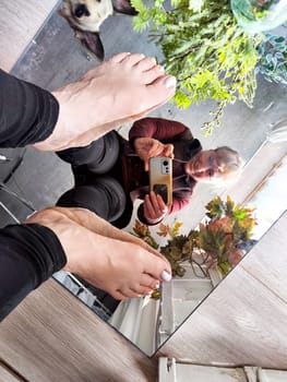 A selfie taken in a mirror, the subject is woman in her home, with plants in the background