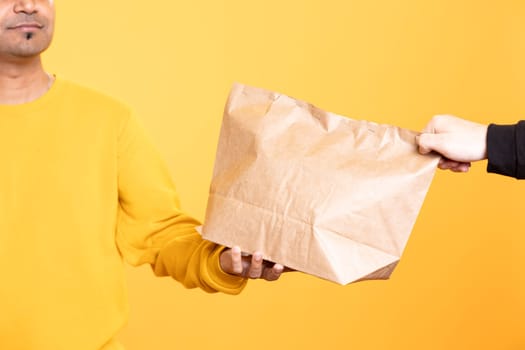 Catering food delivery service employee giving order to client. Close up shot of delivery worker offering lunch paper bag to hungry customer, isolated over studio background