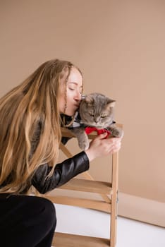 A woman natural blonde long hair smiling in a black clothes sitting on photo studio. girl with pet scottish straight cat. portrait , vertical, close up