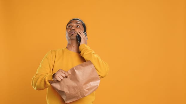 Delivery man arguing with customer on phone after arriving at destination and waiting for him, studio background. Indian person doing deliveries, scolding late client on telephone call, camera A