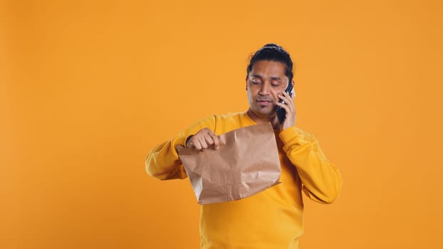 Delivery man arguing with customer on phone after arriving at destination and waiting for him, studio background. Indian person doing deliveries, scolding late client on telephone call, camera B