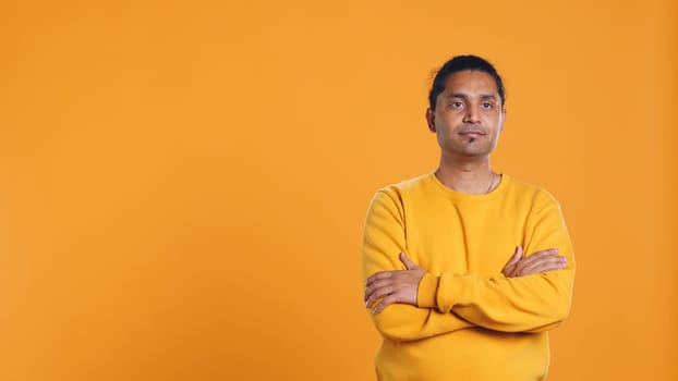 Portrait of cheerful friendly indian man smiling, looking pleased, isolated over yellow studio background. Happy expressive asian person grinning, feeling satisfied, camera B