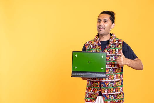 Portrait of joyous man presenting isolated screen laptop, doing thumbs up gesturing, studio background. Happy person doing like hand gesture regarding mockup notebook used for advertising brands