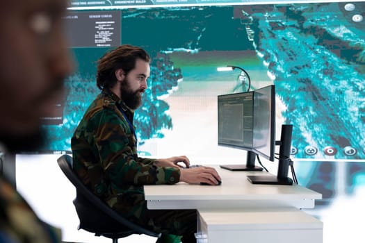 Army IT specialist operating on satellite radar imagery for reconnaissance tasks inside power base monitoring room. Technician gathers intelligence for air force division missions.