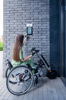 A woman in a wheelchair with an assistive device for manual control enters the entrance. Electric hand bike