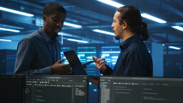 Engineers working in high tech server farm, using laptop and tablet to analyze data, ensuring seamless data flow. Men examining hardware in data center, ensuring system integrity and security