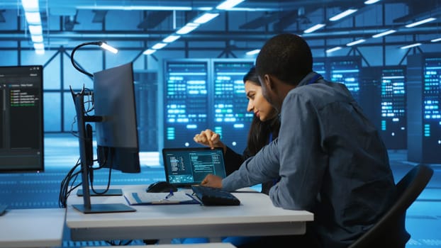 Multiethnic coworkers doing system analysis of server farm supercomputers using tablet. Diverse team of engineers looking at parameters in data center housing storage infrastructure